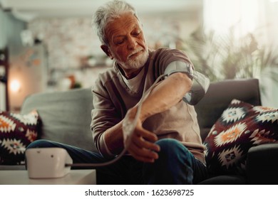 Senior Man Taking His Blood Pressure At Home In The Living Room On Sofa.