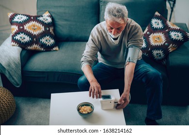 Senior Man Taking His Blood Pressure At Home In The Living Room On Sofa.