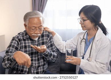 Senior man taking medication while doctor provides assistance and water during home healthcare visit. Elderly care, prescription support, medical treatment, caregiver help concept.