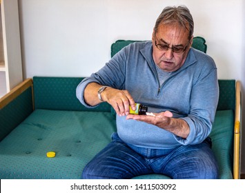 Senior Man Taking Medicine At Home. Older Man Taking Daily Medicine To Consume. Man Pouring A Pill From Into Hand. 