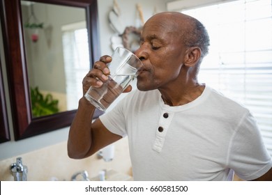 Senior man taking medicine while standing in bathroom at home - Powered by Shutterstock
