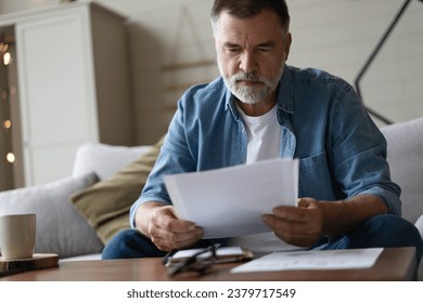 Senior man taking notes in notebook while sitting on the couch, clever gray-haired elderly man writing down thoughts and ideas in notebook - Powered by Shutterstock