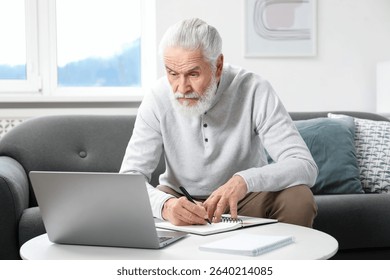 Senior man taking notes while learning online at table indoors. Self-study - Powered by Shutterstock - Get 15% off with code: PIKWIZARD15