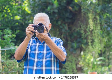 Senior man taking photo by digital camera in the garden. Elderly man wears a blue shirt, happy when using a camera. Photography concept. Space for text - Powered by Shutterstock