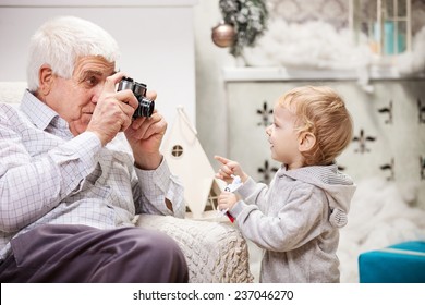 Senior man taking photo of his toddler grandson at Christmas time - Powered by Shutterstock