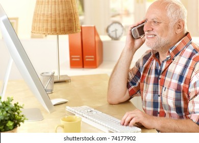 Senior Man Talking On Cellphone, Using Computer, Smiling, Looking At Screen At Home.?