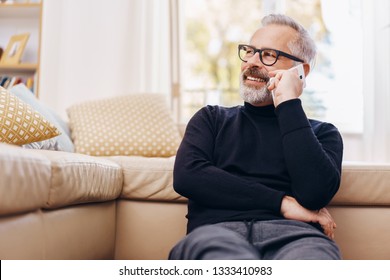 Senior Man Talking On His Mobile Phone At Home Listening To The Call With A Happy Smile As He Relaxes On The Floor In The Living Room