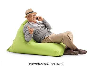 Senior Man Talking On His Cell Phone Seated On A Green Beanbag Isolated On White Background