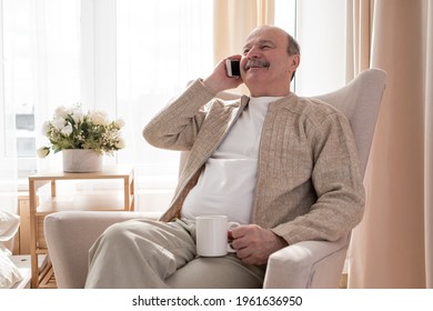 Senior man talking on a mobile phone while relaxing on a sofa in his living room