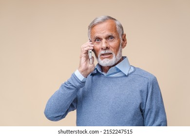 Senior Man Talking Phone, Calling To Somebody, Looking At The Camera With Calm Facial Expression. Indoor Studio Shot Isolated On Beige Background