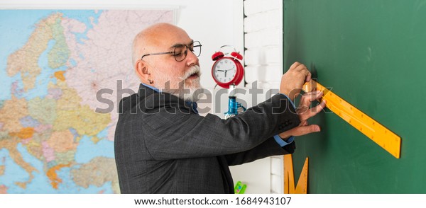 senior man teacher\
use ruler while drawing. tutor man in glasses draw with ruler on\
blackboard. back to school. what angle you look. geometric shapes.\
high school modern\
education.