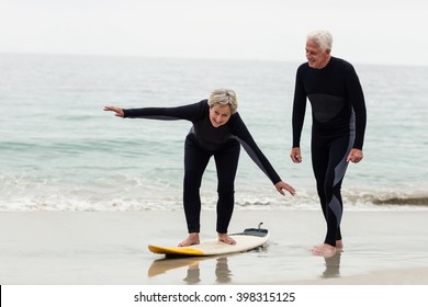 Senior Man Teaching Woman To Surf On Beach