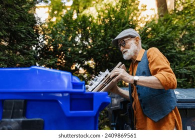 Senior man throwing paper waste, cardboards into recycling container in front apartment. Elderly man sorting the waste according to material into colored bins. - Powered by Shutterstock