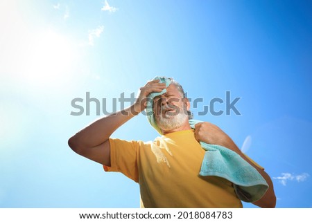 Senior man with towel suffering from heat stroke outdoors, low angle view