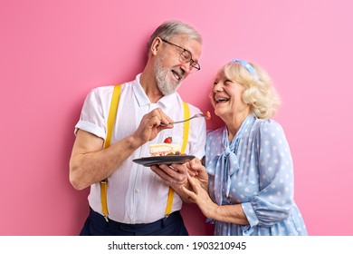 senior man treats a woman with a cake, elderly couple celebrating birthday or anniversary, isolated on pink background, portrait - Powered by Shutterstock