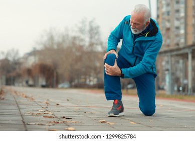 The senior man use hands hold on his knee while running outdoor