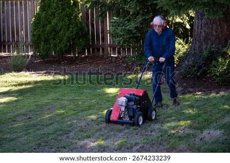 Senior man using an aerator machine to improve grass lawn health by reducing compaction, yard and garden maintenance equipment
