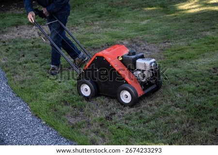 Senior man using an aerator machine to improve grass lawn health by reducing compaction, yard and garden maintenance equipment
