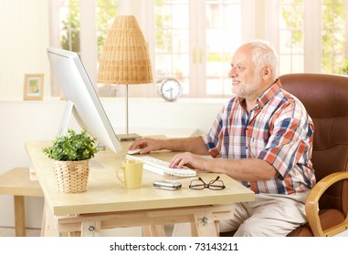 Senior Man Using Desktop Computer At Home, Looking At Screen, Smiling.?