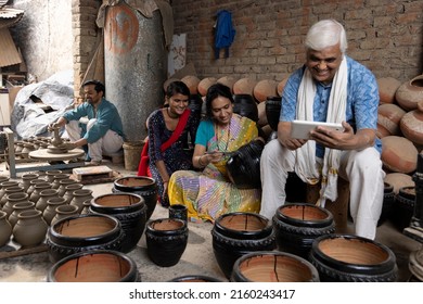 Senior man using digital tablet while his family is manufacturing and painting clay pots at workshop - Powered by Shutterstock