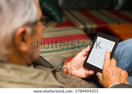 Senior man using an ebook reader in the sofa