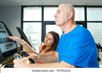 Senior Man Using Electronic Exercise Machine Under Supervision