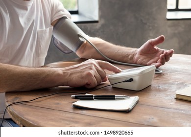 Senior Man Using A Home Blood Pressure Machine To Check His Health Sitting At Living Room