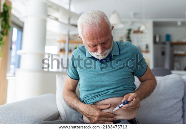 Senior man using lancet pen at\
home. Diabetes control Mature man sitting and injecting\
insulin