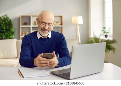 Senior man using mobile phone. Happy retired man in glasses sitting at desk with laptop and cellphone, paying bills online, reading news, sending emails, making banking transaction, calling his