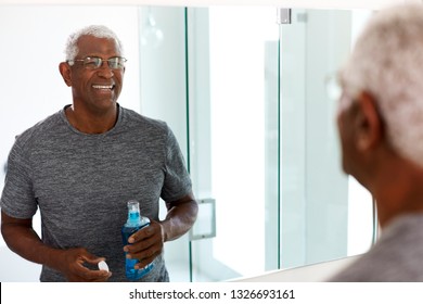 Senior Man Using Mouthwash Looking At Reflection In Bathroom Mirror Wearing Pajamas - Powered by Shutterstock