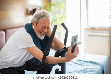 Senior man using smartphone on exercise bike at home - Powered by Shutterstock