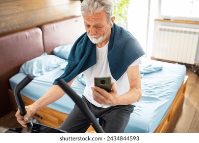 Senior man using smartphone on fitness bike at home - Powered by Shutterstock