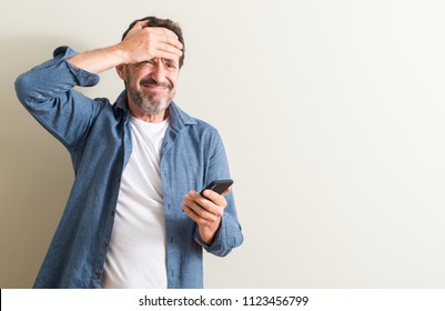 Senior man using smartphone stressed with hand on head, shocked with shame and surprise face, angry and frustrated. Fear and upset for mistake. - Powered by Shutterstock