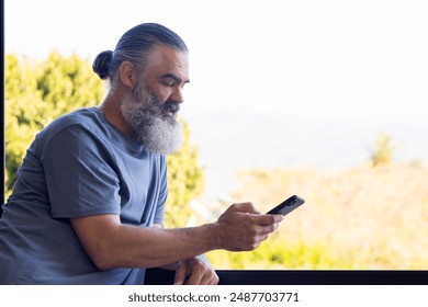 Senior man using smartphone while leaning on balcony railing, enjoying outdoors, copy space. Technology, elderly, lifestyle, relaxation, mobile, communication - Powered by Shutterstock