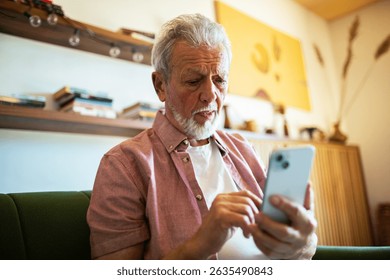 Senior man using smartphone while sitting on couch at home