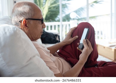 Senior man using smartphone while relaxing indoors, concept of elderly lifestyle, digital communication, technology for seniors, online connection, health, and modern retirement life.