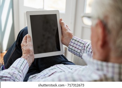 Senior Man Using Tablet Computer At Home, Over Shoulder View