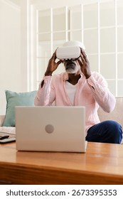 Senior man using VR headset while sitting on sofa with laptop nearby. Technology, virtual reality, leisure, innovation, gadgetry, digital