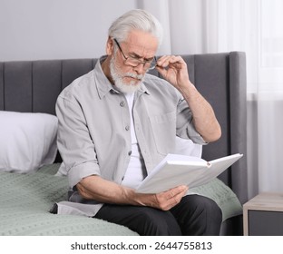 Senior man with vision problem reading book on bed at home