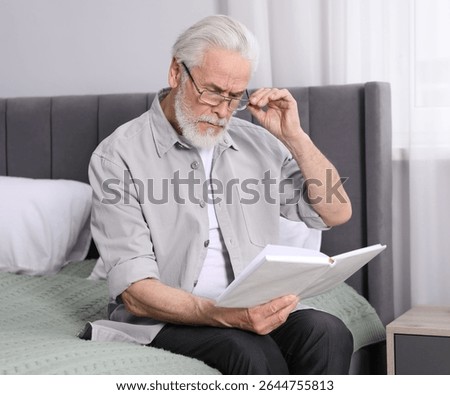 Senior man with vision problem reading book on bed at home