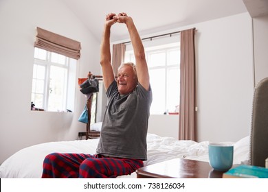 Senior Man Waking Up And Stretching In Bedroom