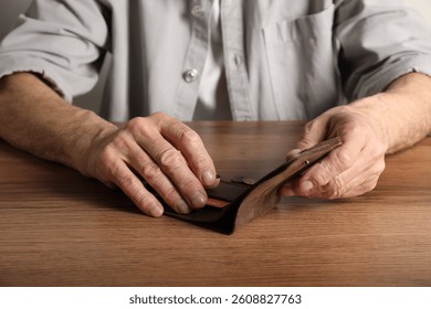 Senior man with wallet counting coins at wooden table, closeup. Financial problems