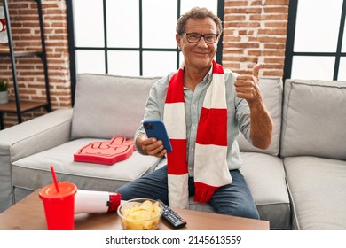 Senior Man Watching Football Looking At Smartphone Smiling Happy And Positive, Thumb Up Doing Excellent And Approval Sign 