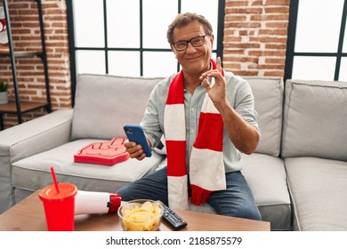 Senior Man Watching Football Looking At Smartphone Surprised With An Idea Or Question Pointing Finger With Happy Face, Number One 