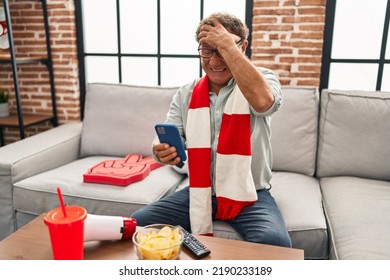 Senior Man Watching Football Looking At Smartphone Stressed And Frustrated With Hand On Head, Surprised And Angry Face 