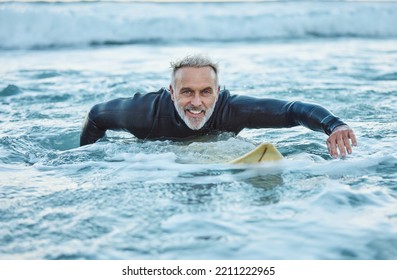 Senior man, water and sports surfer on a beach with smile training for fitness and health or hobby in the outdoors. Elderly male paddling on surfboard for healthy exercise in the ocean waves at sea - Powered by Shutterstock