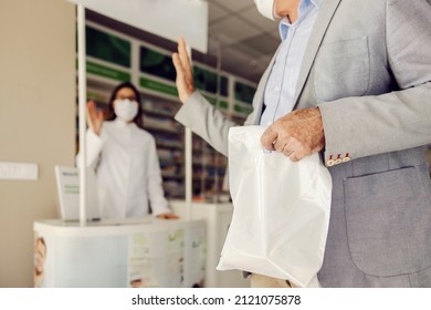 A Senior Man Waving To A Pharmacist And Leaving Store With Medicines.