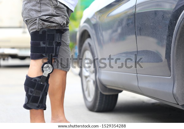 Senior man wear knee\
support brace on leg standing at the car parking lot, Medical and\
healthcare concept 