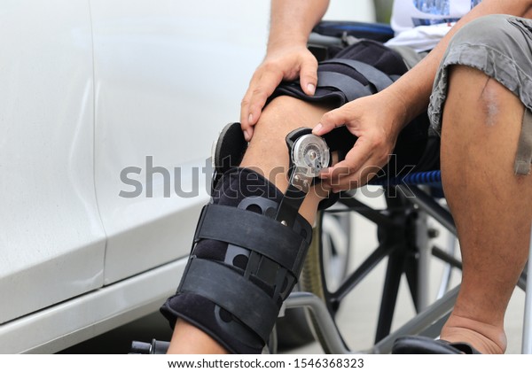 Senior man wear knee\
support brace on leg standing at the car parking lot, Medical and\
healthcare concept