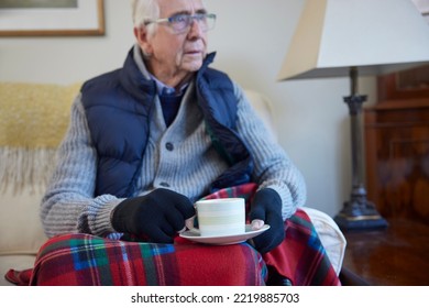 Senior Man Wearing Extra Clothes With Hot Drink Trying To Keep Warm At Home In Energy Crisis - Shutterstock ID 2219885703